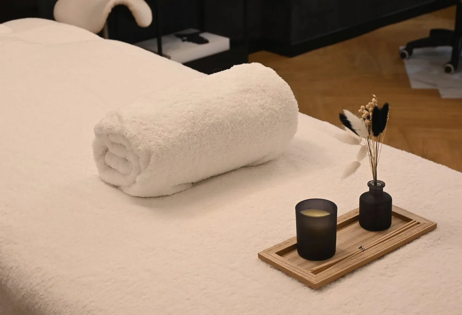 Rolled white towel, a candle and a small vase on a treatment table