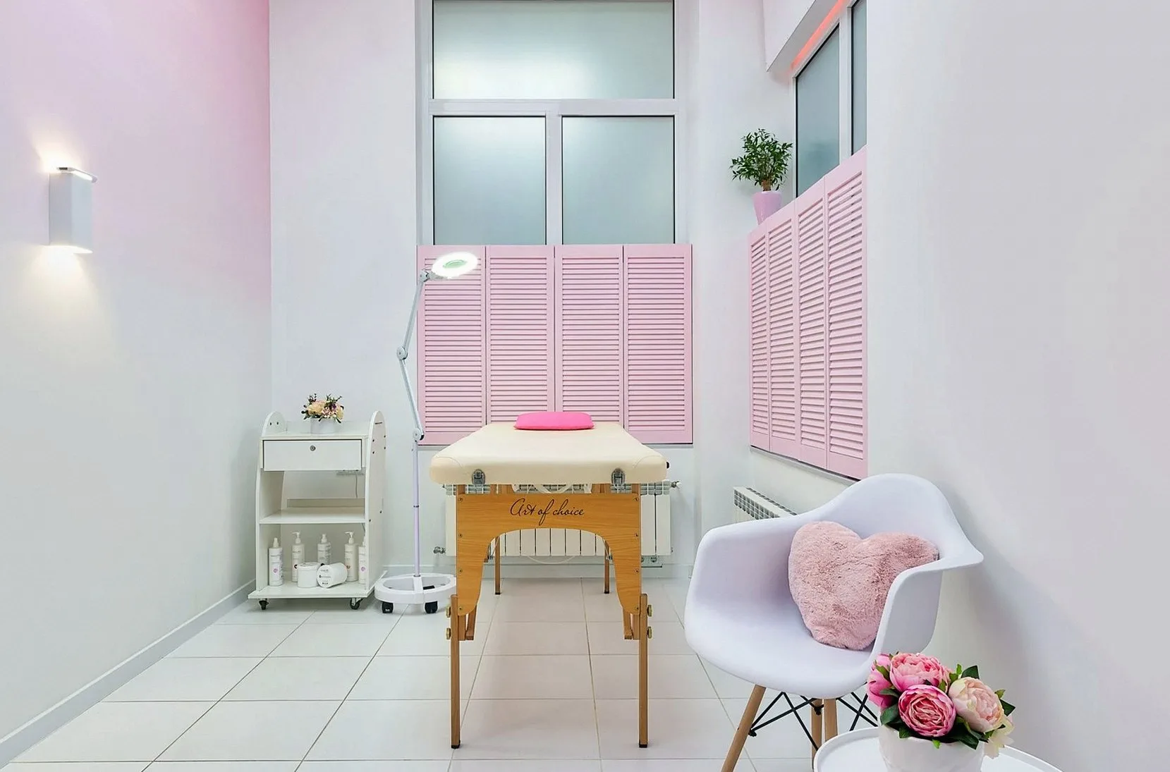 Bright treatment room with a massage table, a white armchair and pink blinds