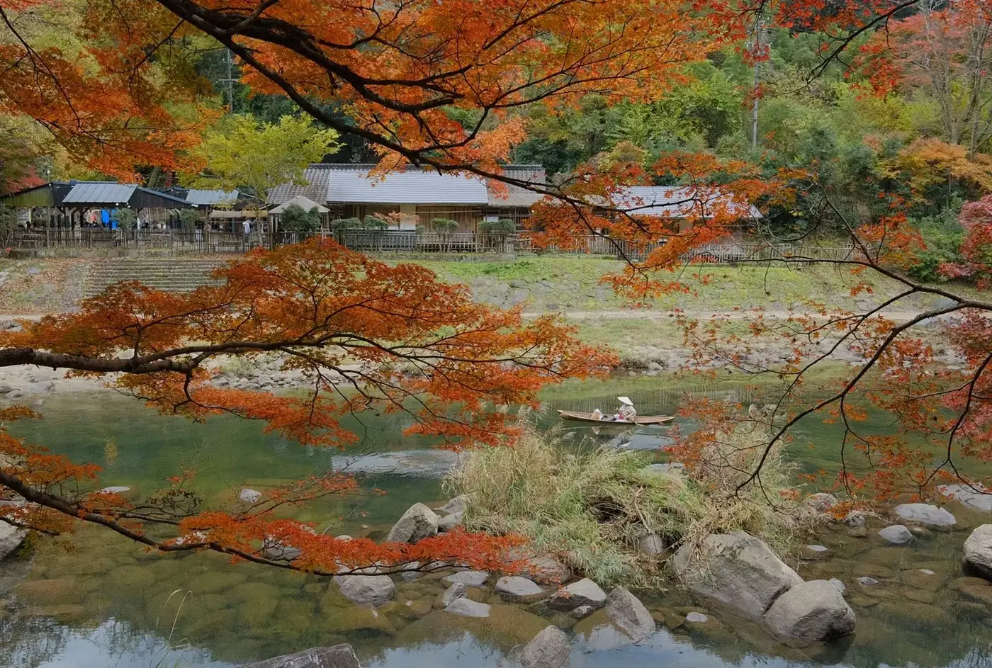 Red autumn maple leaves over a pond with a house on the far bank
